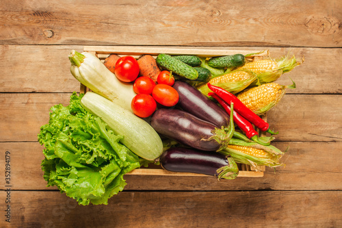 Wooden box with fresh vegetables on a wooden background. Good harvest concept, natural product. Flat lay, top view