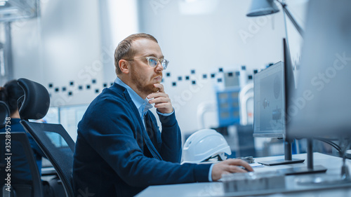 Shot of Male Industrial Engineer Solving Problems, Working on a Personal Computer, He is Working in Office in Modern Factory with High-Tech Machinery.