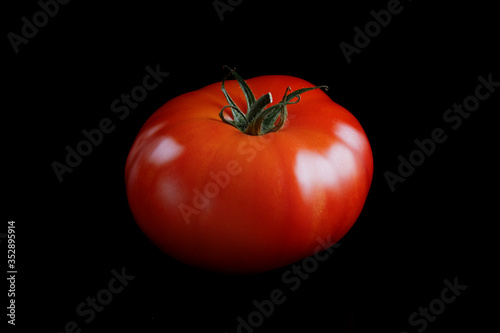 Fresh bright red ripe beefsteak tomato with green stalk on a black background