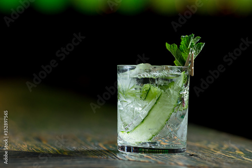 alcoholic cocktail with mint cucumber and liquor in a transparent glass on a dark background with color highlight with bar shots