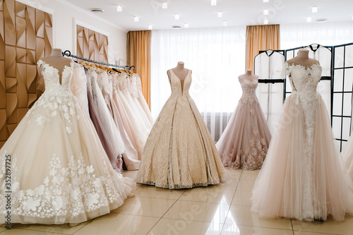 Beautiful wedding dresses, bridal dress hanging on hangers and mannequin in studio. Fashion look. Interior of bridal salon. photo