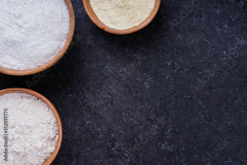 Dark marble background with different sorts of flour in wooden bowls. Baking ingredients with space for text or image. Flat lay top view, studio shot