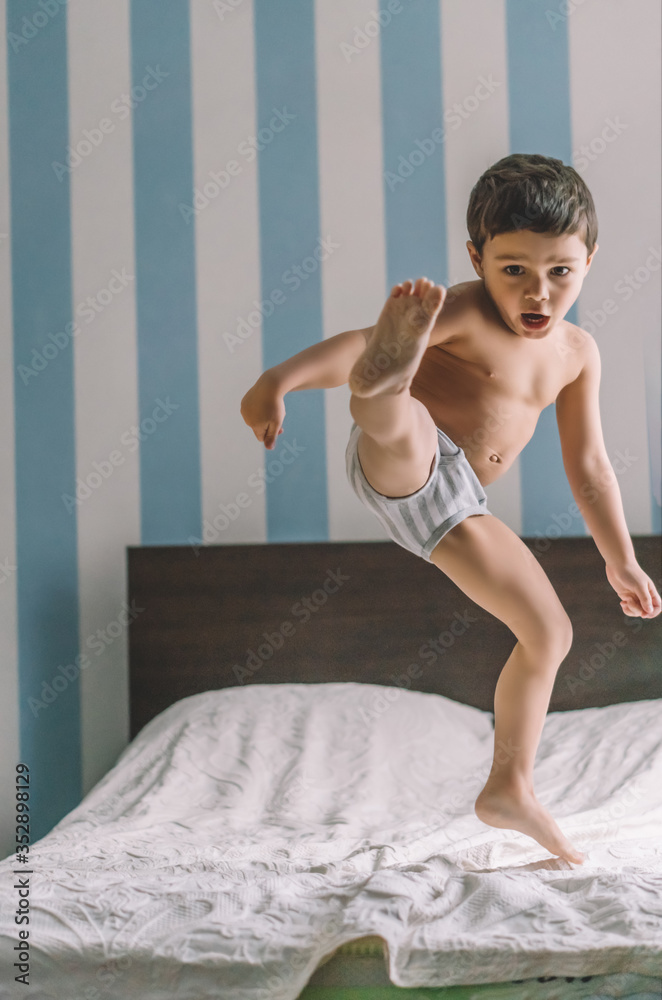 cute boy having fun while jumping and kicking with leg on bed Stock .