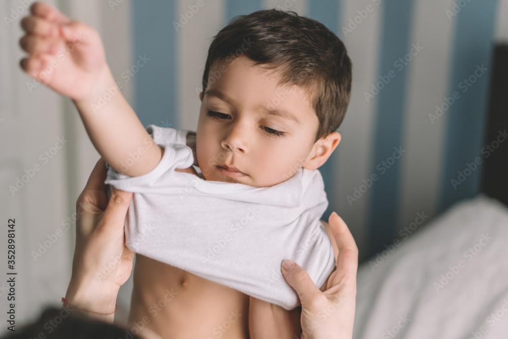 cropped view of woman putting singlet on adorable son - obrazy, fototapety, plakaty 