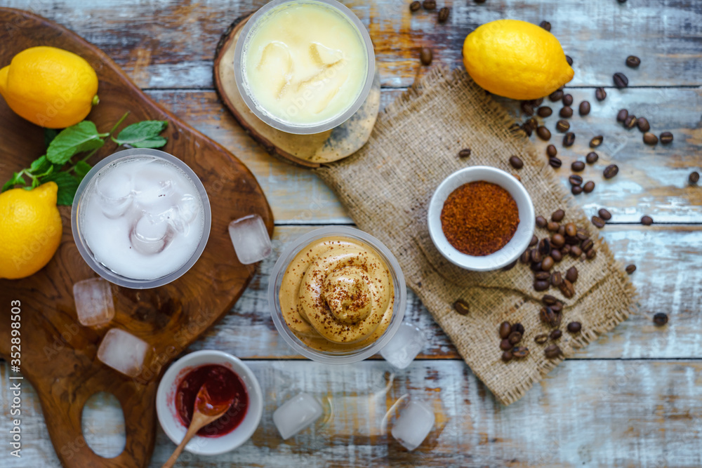 Dalgona coffee and other cold drinks are arranged randomly alongside some basic ingredients, such as coffee beans, lemons, jams, ice cubes and sugar. Dalgona coffee and other cold drinks are arranged randomly alongside some basic ingredients, such as coffee beans, lemons, jams, ice cubes and sugar.
