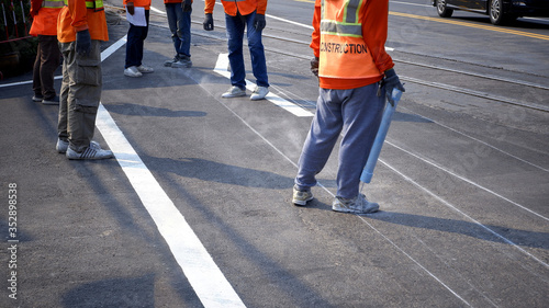 Low section of road workers group are working to marking line for painting traffic color lines on asphalt road with railway track crossing on street surface in the city, selective focus
