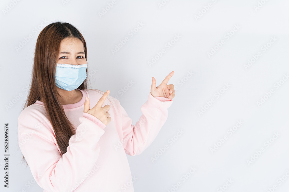 Asian beautiful happy hipster woman wearing a medical protection face mask for protect the coronavirus, filter dust PM 2.5 and cold and her finger pointing outside on the white background Asian beautiful happy hipster woman wearing a medical protection face mask for protect the coronavirus, filter dust PM 2.5 and cold and her finger pointing outside on the white background