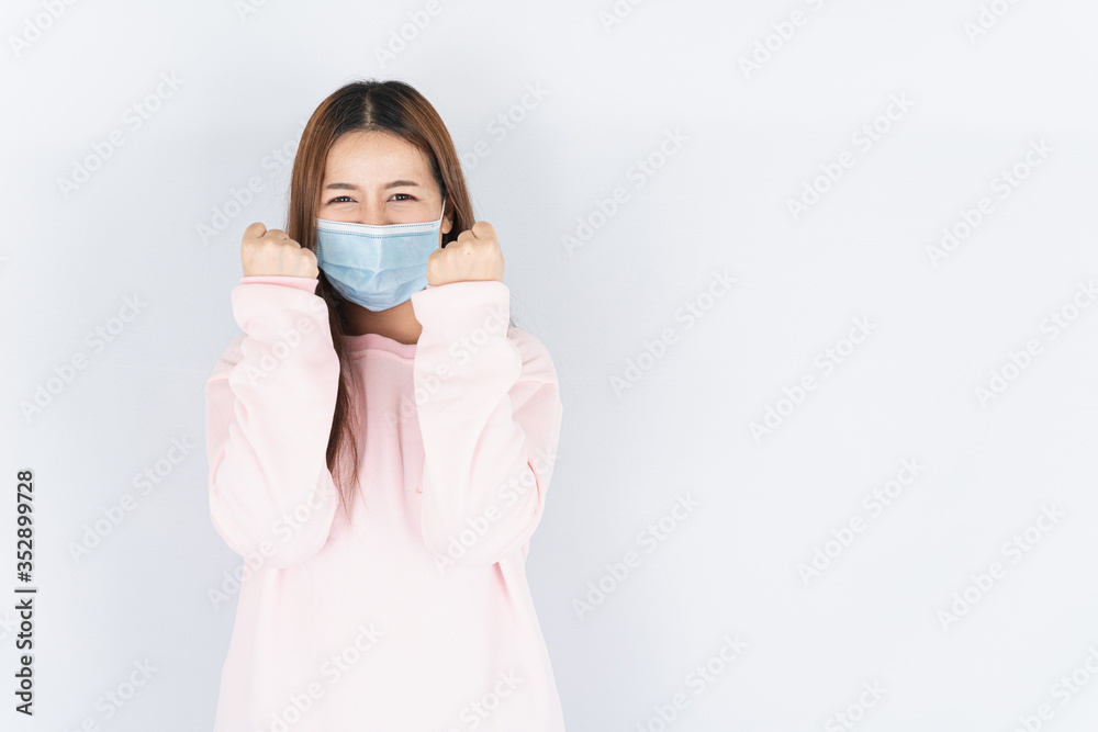 Asian beautiful happy hipster woman wearing a medical protection face mask for protect the coronavirus, filter dust PM 2.5 and cold and raise her hand to fight them on white background Asian beautiful happy hipster woman wearing a medical protection face mask for protect the coronavirus, filter dust PM 2.5 and cold and raise her hand to fight them on white background