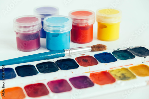 Colorful gouache paints and brush for painting on white wooden table. Copy, empty space for text