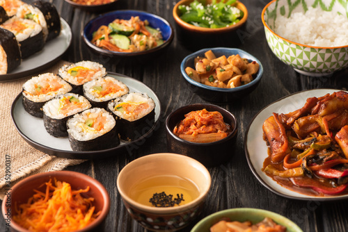 selective focus of traditional gimbap and kimchi near tasty korean dishes on wooden surface