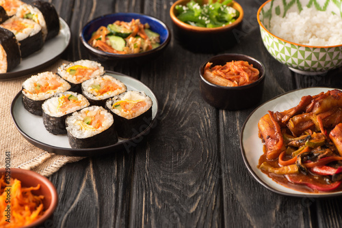 selective focus of traditional gimbap near tasty korean dishes on wooden surface