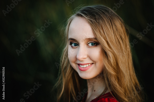 Portrait of a beautiful girl stand in autumn in a red dress against the background of the field on the nature. upper half. look straight ahead. Close up. headshot.