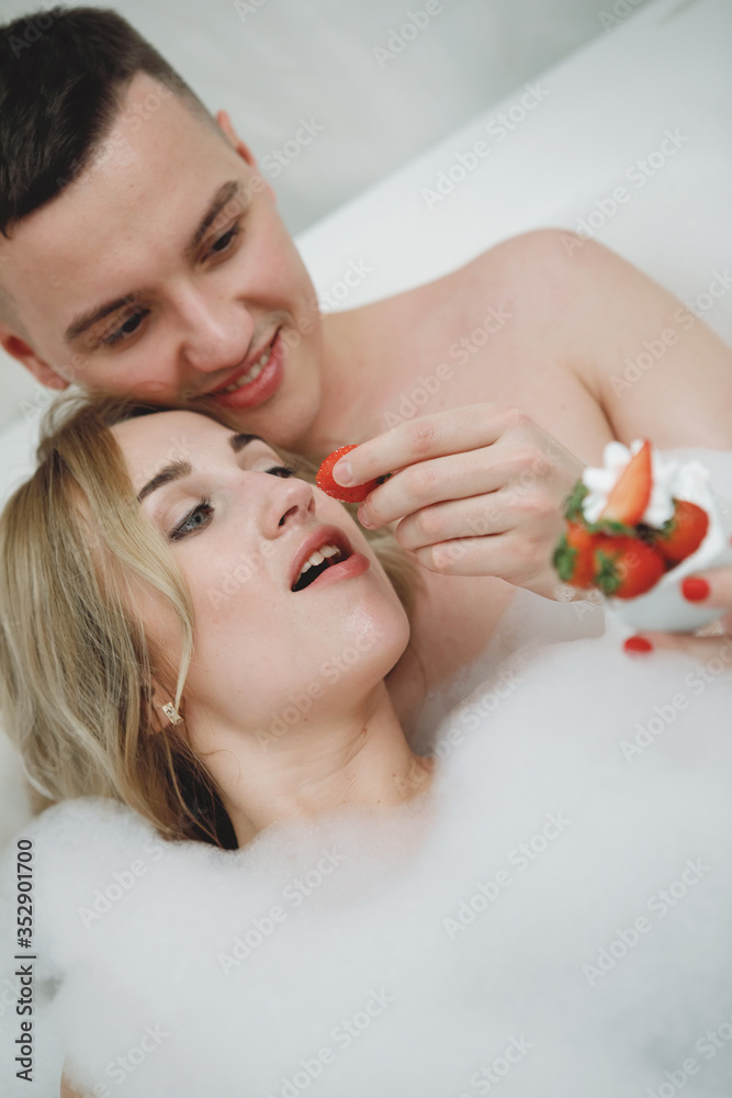 Loving couple in a bath with strawberries.