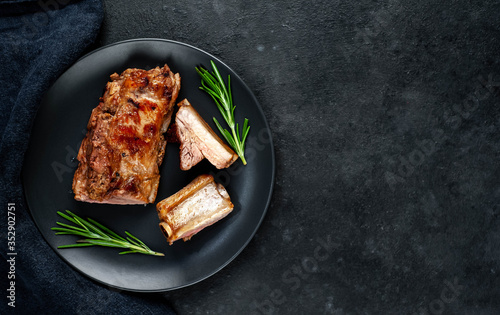 Grilled pork ribs on a black plate with spices on a stone background with copy space for your text
