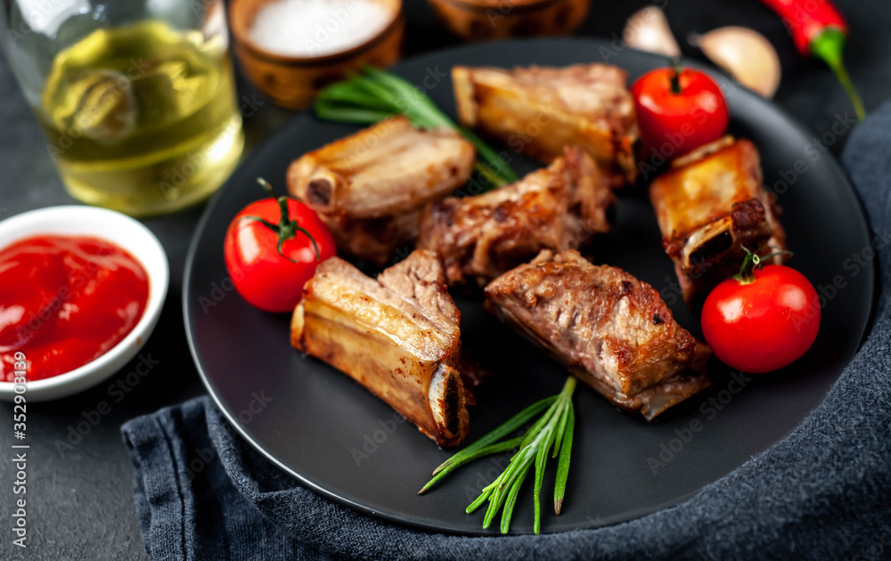 Grilled pork ribs on a black plate with spices on a stone background Grilled pork ribs on a black plate with spices on a stone background