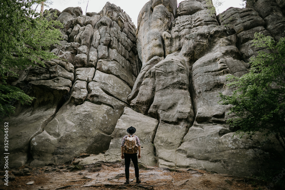 Hiker with backpack looks at high cliff in mountains, travel concept Hiker with backpack looks at high cliff in mountains, travel concept