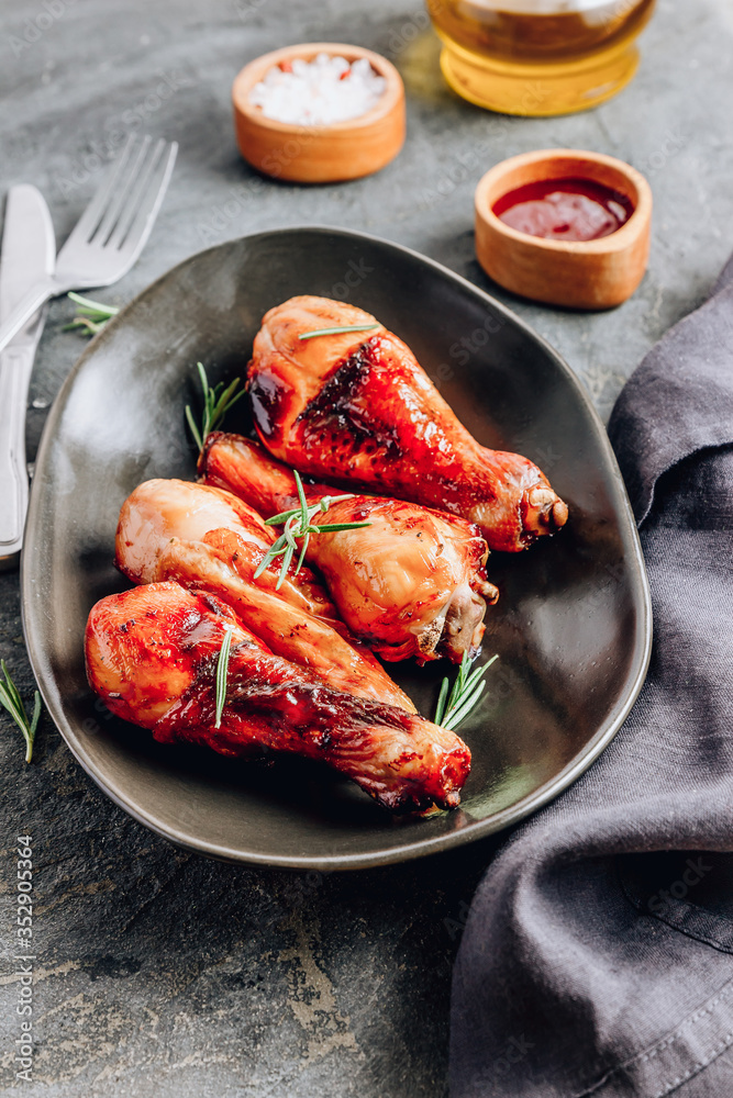 Chicken legs on black plate with red sauce and rosemary on black rustic background. Chicken legs on black plate with red sauce and rosemary on black rustic background.