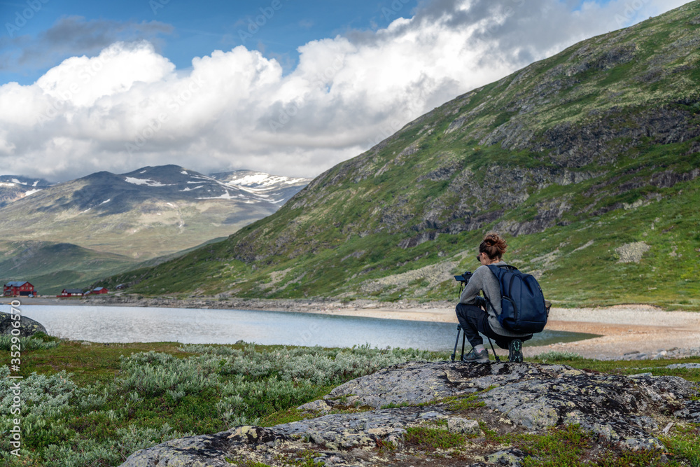 Fototapeta premium Young woman traveler professional photographer takes a picture of the landscape on the camera on a tripod, Norway, beautiful northern nature