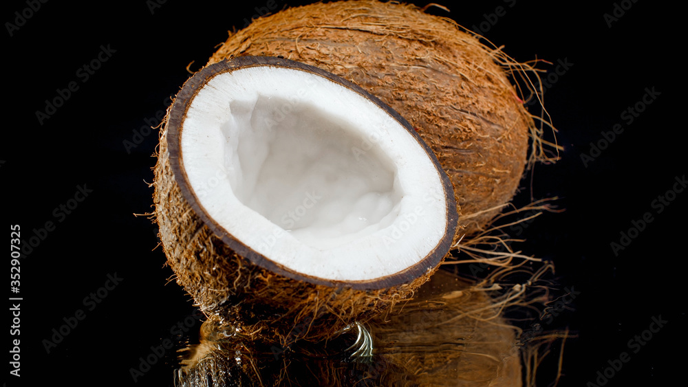 Closeup image of broken in halves coconut against black background. Abstract background of exotic tropical fruits and nuts Closeup image of broken in halves coconut against black background. Abstract background of exotic tropical fruits and nuts