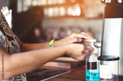 Woman uses her hand to press hand sanitizer bottle to clean her hand in coffee shop. Hand sanitizer alcohol gel rub clean hands hygiene prevention of coronavirus (Covid-19) virus outbreak.