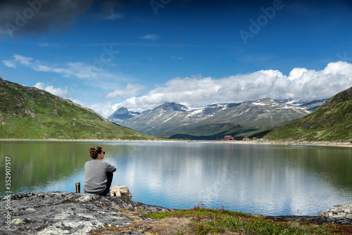 Young woman traveler sits on a lake with mountains and hills, traveling, beautiful northern landscape © olezzo