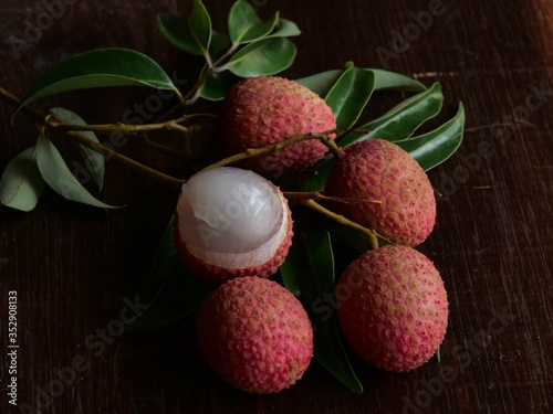 Red lychee fruits and green leaves on a wooden table background, dark tones. Has a pleasant aroma and a thirst-quencher, high vitamin C.