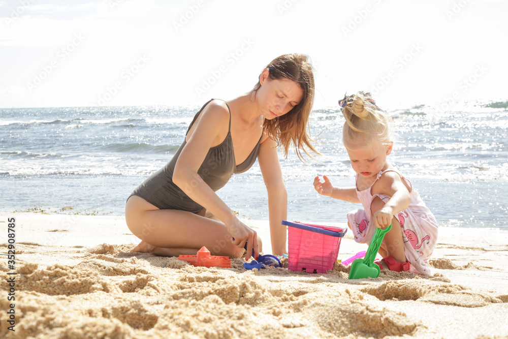 Summer vacation. Adorable toddler girl and her mother playing with beach toys on the sandy beach. Summer vacation. Adorable toddler girl and her mother playing with beach toys on the sandy beach.