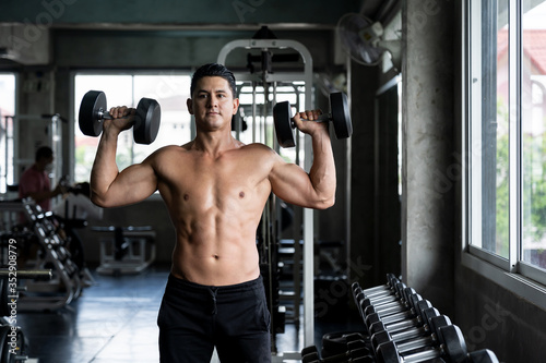 Handsome man standing with beautiful muscular lifting dumbbells in the fitness gym. Man exercising in the sports center. Man taking care of his health dumbbells