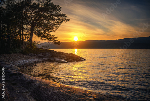 Bright beautiful landscape, sunset on Lake Snasa in Norway. Stone coast and tree silhouette