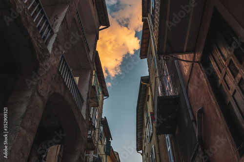A picturesque low angle view of old tall apartment buildings in a French medieval village and blue sky with clouds illuminated by warm sunlight during sunset (Puget-Theniers, Alpes-Maritimes, France)