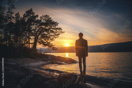 Young woman stands with her back on the lake at sunset and looks at the sun