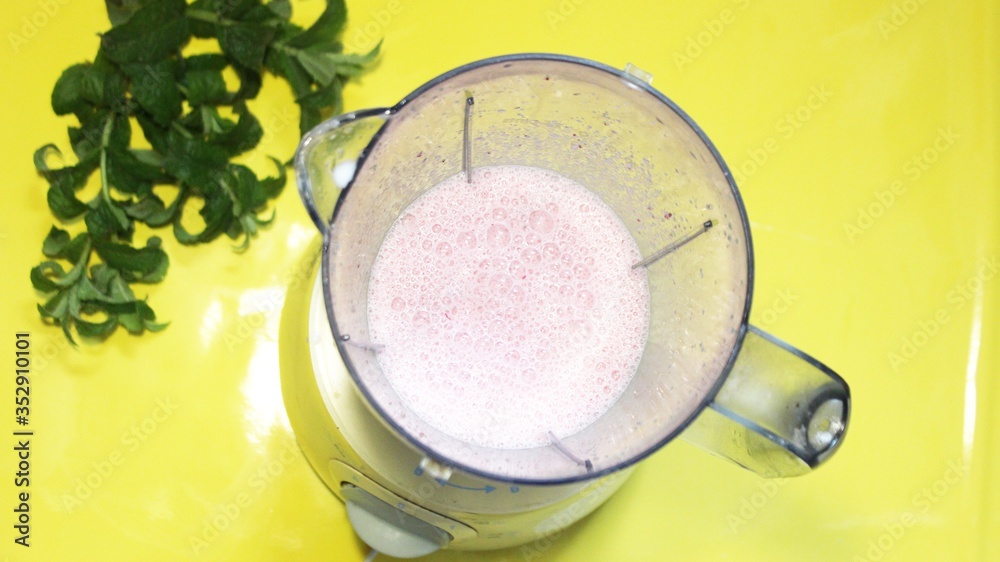 Milk smoothie is mixed in a mixer on a yellow background with mint. milk are mixed in a blender on the table. View from above. Summer fresh cocktail mixed in a blender