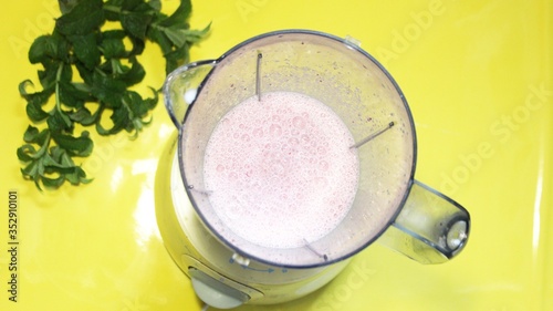 Obraz na płótnie Milk smoothie is mixed in a mixer on a yellow background with mint. milk are mixed in a blender on the table. View from above. Summer fresh cocktail mixed in a blender w salonie