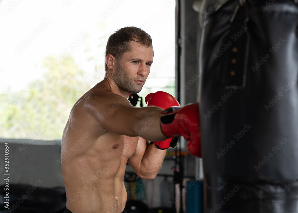 Muscular man boxer wearing red boxing glove and hitting a black punching a boxing bag at the boxing gym, Exercising and workout in the fitness sport gym concept