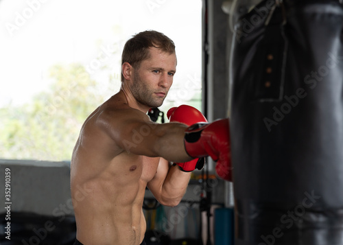 Muscular man boxer wearing red boxing glove and hitting a black punching a boxing bag at the boxing gym, Exercising and workout in the fitness sport gym concept © amorn