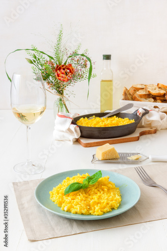 Risotto Milanese, wooden table with traditional Italian saffron risotto, glasses and pitcher of wine, bottle of olive oil, basket of bread and flowers, lunch for 2 people .