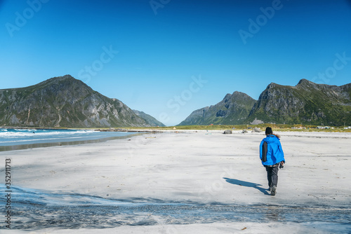 Young woman traveler in a blue jacket is walking along the north beach. Beautiful landscape. Lofoten islands in Norway