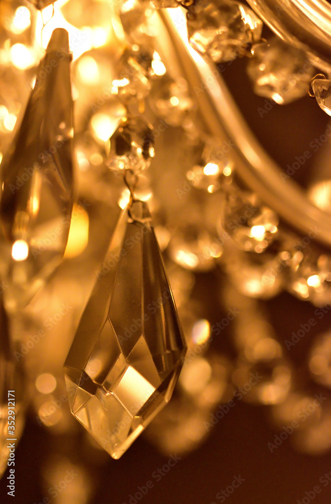 Detail of crystal ornaments on antique chandelier. Warm white color balance. Vertical photo.