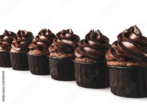 Delicious chocolate cupcakes with gold sparkles sprinkled on chocolate icing lined up diagonaly on isolated white background. Mockup for your design. Close-up. Place for text. photo