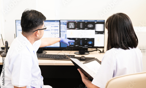 Asian radiologists shows the patient CT scan and discussion treatment patient information to doctor in x-ray room.High technology for planing medical treatment equipment concept. photo