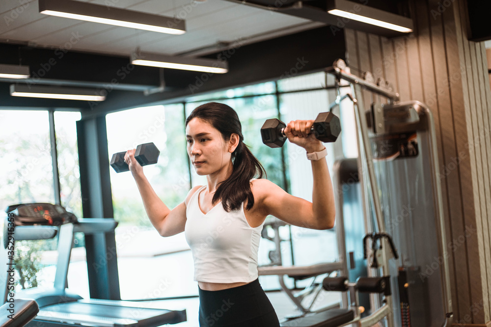 Fototapeta premium Young beautiful slim woman doing exercises with dumbbell in gym