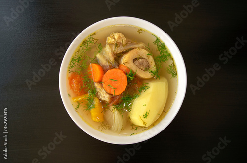 Shurpa soup in a white bowl on dark wooden background. Top view. Famous traditional Asian, Uzbek, Middle East soup with beef or lamb and vegetables. Shorpa, sherpa, chorba