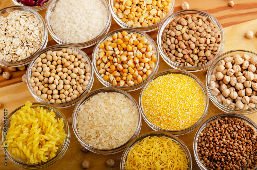 Flat lay view at set of various legumes and grains in glass bowls on wooden kitchen table, non-perishable, long shelf life food concept