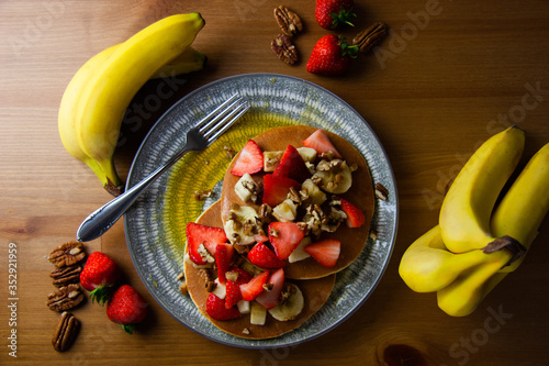 Indulgent banana strawberry and peacan nuts pancakes on a rustic wooden background top view flatlay- with whole bananas bunch and whole nuts and strawberries, hot and delicious homecooked brunch photo