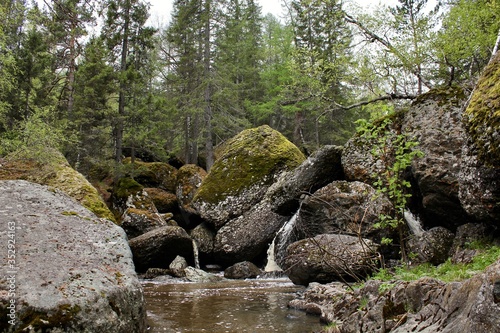 A mountain river waterfall flows through a river bed through huge boulders with moss
