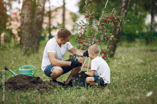 Family on a yard. Father with son planting a tree. Boy with a green funnel © prostooleh