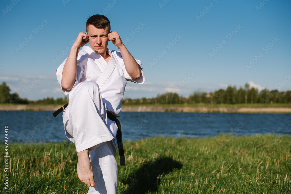 A man karate fighter in white kimono training outdoor in the park A man karate fighter in white kimono training outdoor in the park