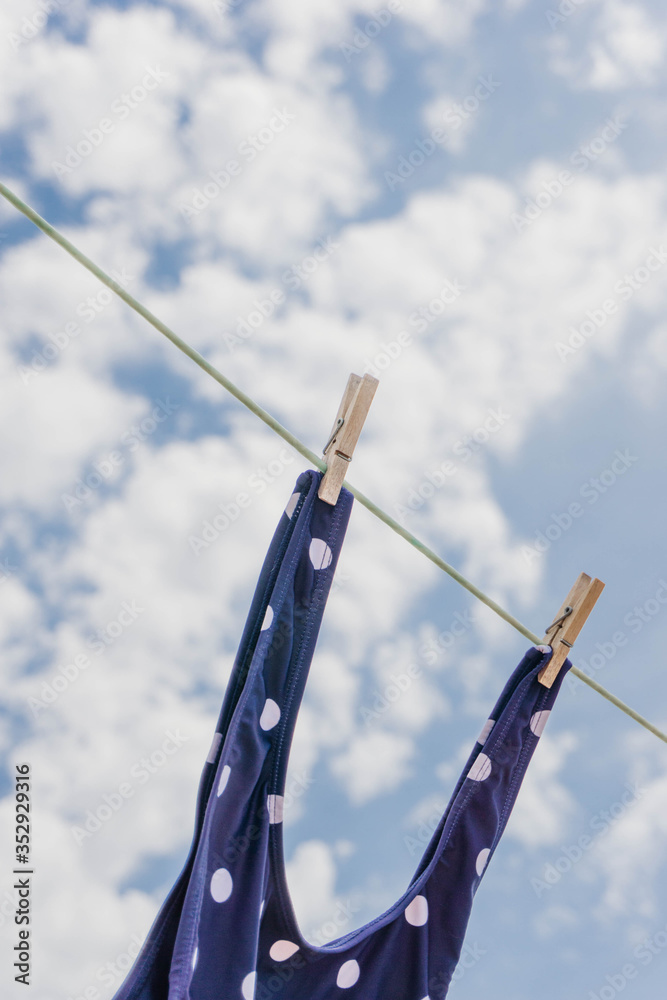 Close up view of a cute swimsuit strap hanging in a clothes line with a clothespine against blue sky. Close up view of a cute swimsuit strap hanging in a clothes line with a clothespine against blue sky.