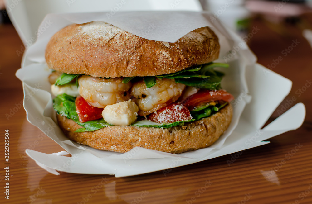 hamburger with dark flour with vegetables and shrimp on a wooden background hamburger with dark flour with vegetables and shrimp on a wooden background