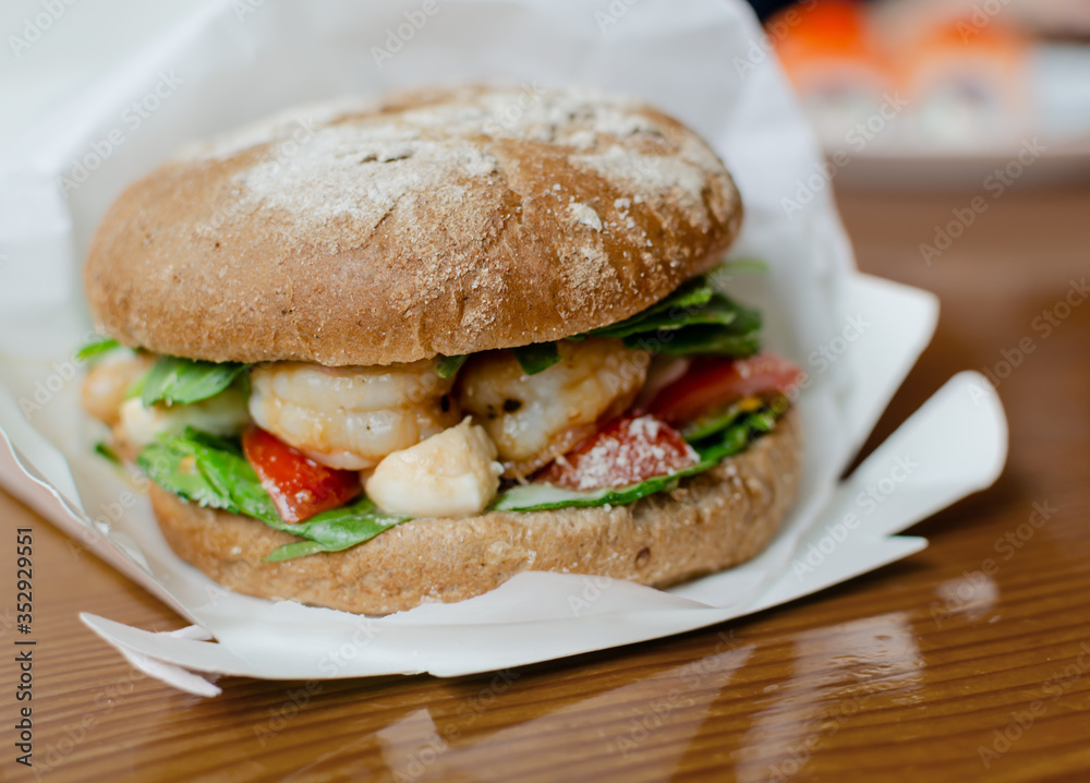 hamburger with dark flour with vegetables and shrimp on a wooden background hamburger with dark flour with vegetables and shrimp on a wooden background